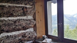 Een rustiek houten interieur met een houten wand, een raam met uitzicht op een berglandschap, en een kleine tafel met een kopje en een boek.