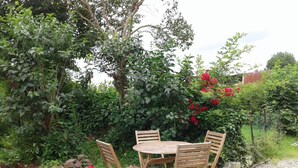Un jardín con una mesa redonda de madera y cuatro sillas, rodeado de grava y follaje.