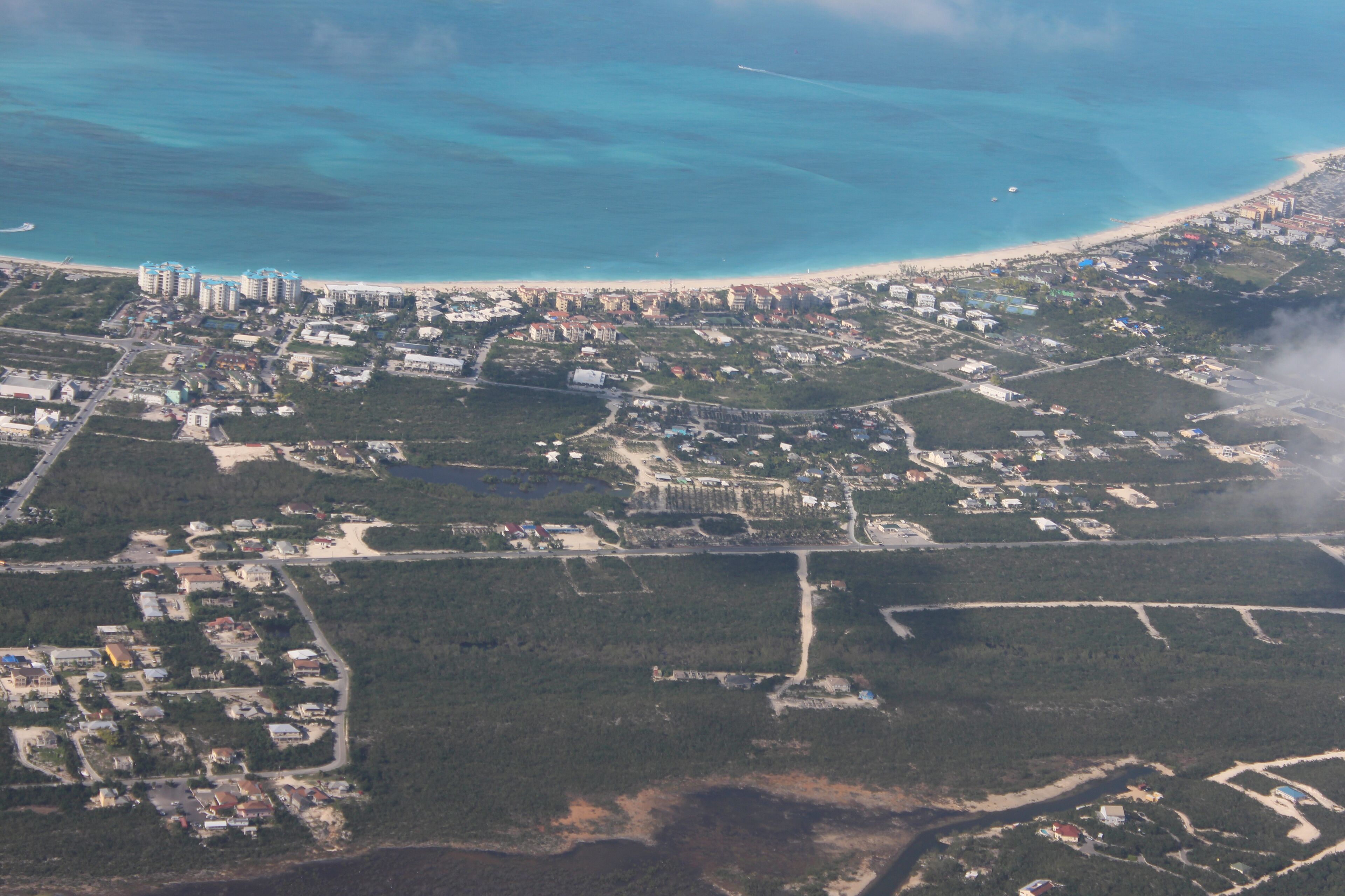 An aerial view of a coastal town with dense residential areas, a beach, and a marina.