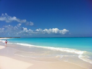 A beach with clear turquoise water and a person walking on the sand.