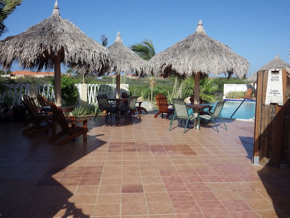 A poolside area with thatched umbrellas, lounge chairs, and a pool.
