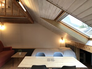 A modern interior with a sloped ceiling, a dining table with chairs, a sofa, and a small table with a plant. - Joli studio 4P entre télécabine et Commerces (Cauterets)
