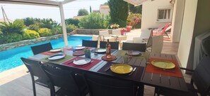 Un espace de restauration en plein air avec vue sur la piscine, comprenant une table dressée avec des assiettes, des couverts et des verres, entourée de chaises.