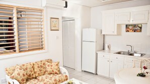 A compact kitchen with white cabinets, a white refrigerator, and a dining area with a white table and chairs. - Your Home Away From Home (Rodney Bay)
