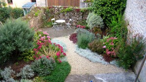 Ein Garten mit Steinmauer, Kiesweg und einer Sitzgelegenheit mit Stühlen und Tisch.