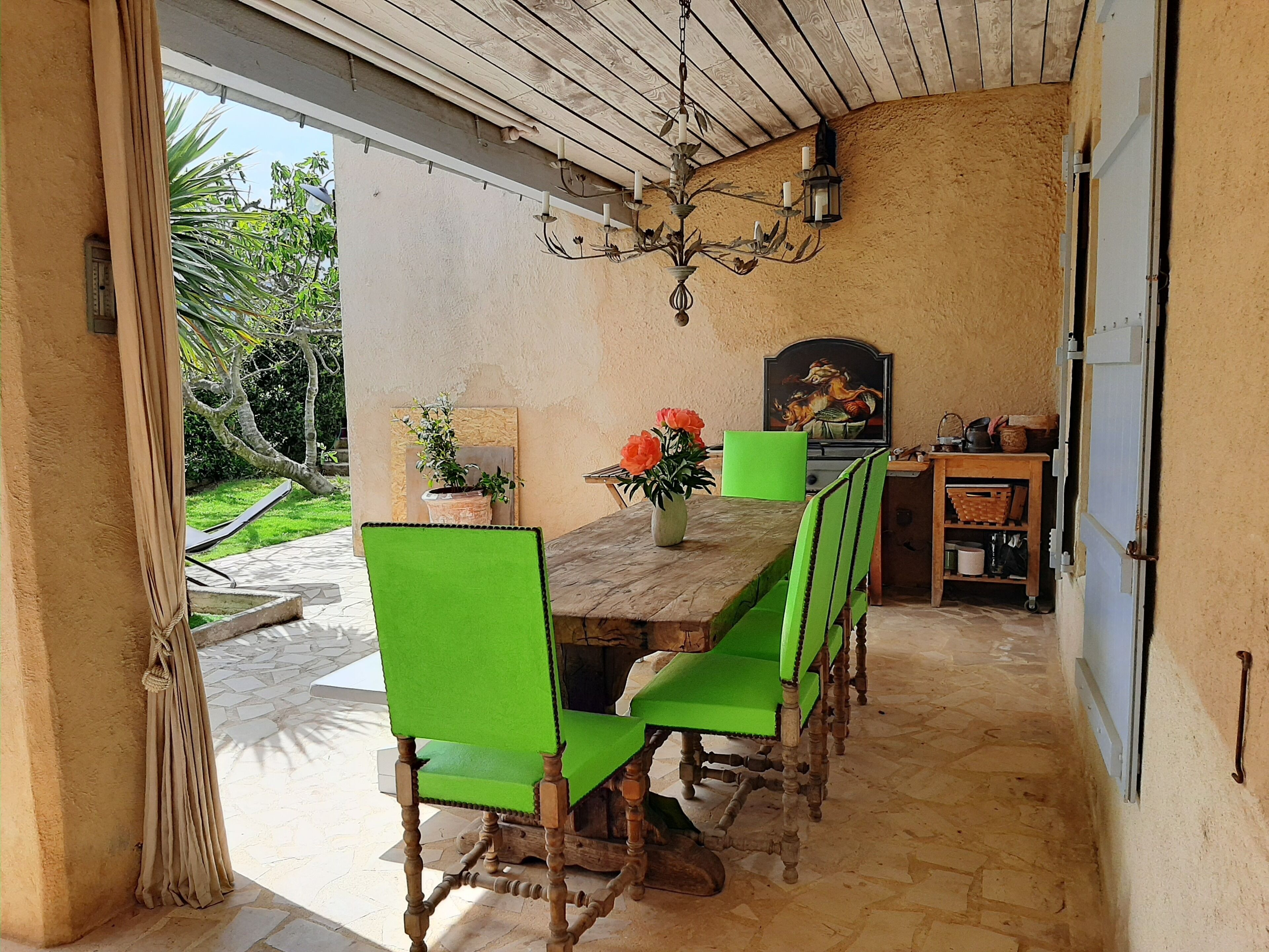 A dining area with a wooden table, green chairs, a chandelier, and a painting on the wall.