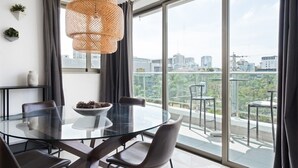 Ein moderner Essbereich mit einem Glastisch und Stühlen, einer gewebten Pendelleuchte und Blick auf die Stadt durch große Fenster.