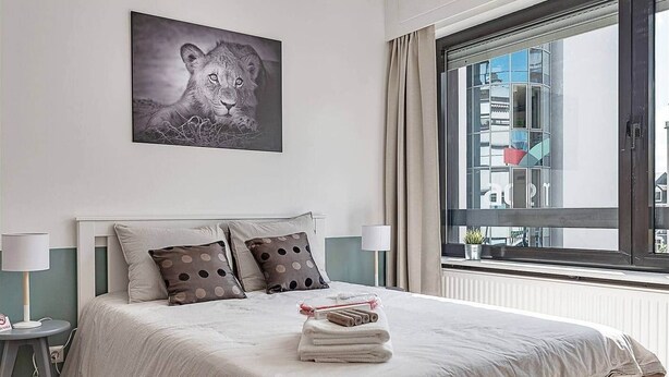 Une chambre d’hôtel avec un grand lit, deux tables de chevet, une fenêtre avec des rideaux et un tableau encadré au mur.