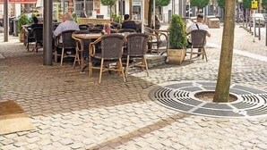 Un café en plein air avec des tables et des chaises sous des parasols, entouré de pavés et de bâtiments.