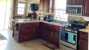 A kitchen with wooden cabinets, a stove, a microwave, and a ceiling fan. - 
2 BEDROOMS WITH OCEAN VIEW AND GARDEN VIEW IN JOST VAN DYKE – SUNRISE (Jost Van Dyke)