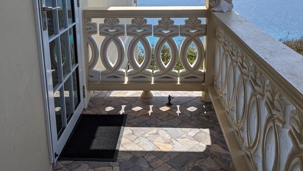 A balcony with a stone floor, a decorative railing, and a view of the sea and hills. - 
2 BEDROOMS WITH OCEAN VIEW AND GARDEN VIEW IN JOST VAN DYKE – SUNRISE (Jost Van Dyke)