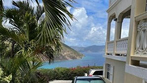 A vehicle parked in a driveway with a view of the ocean and hills in the background. - 
2 BEDROOMS WITH OCEAN VIEW AND GARDEN VIEW IN JOST VAN DYKE – SUNRISE (Jost Van Dyke)