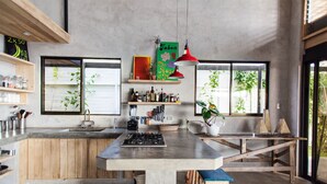 Una cocina moderna con una isla central, estantes de madera y ventanas amplias.