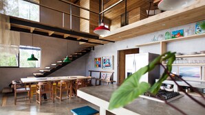 Una cocina amplia con vigas de madera, un comedor con una mesa larga y sillas, y una escalera que sube a un nivel superior.