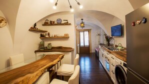 Een keuken met houten aanrecht, een eethoek met een houten tafel en stoelen, een wasmachine en een aan de muur bevestigde televisie.