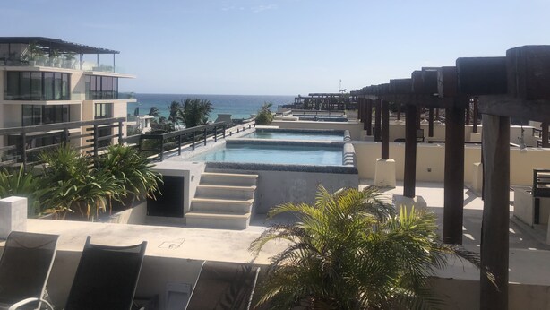 A resort pool area with a view of the ocean, a staircase leading to a deck, and palm trees. - Aldea Thai Penthouse  2br big private roof top & private pool by oceanfront  (Playa del Carmen)