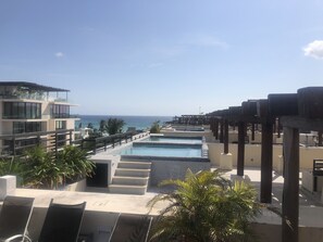 A resort pool area with a view of the ocean, a staircase leading to a deck, and palm trees.