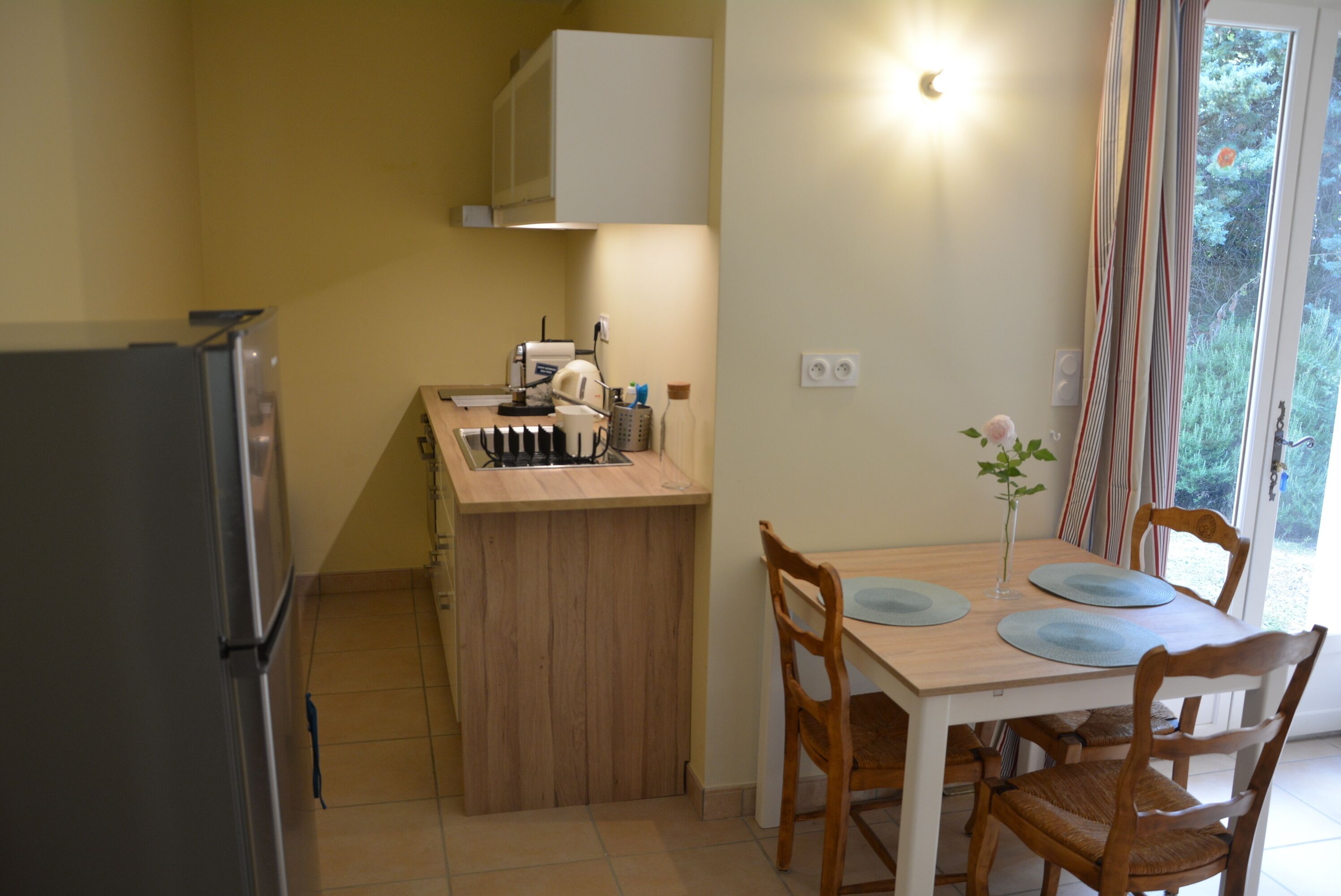 A compact kitchen with a refrigerator, a small island with a sink, and a dining table with chairs.