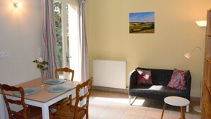 A dining area with a table, chairs, and a window with curtains. There is a sofa and a lamp in the living area. - Vacation rental for 3 people, 1 bedroom, pool, nature and peace and quiet guaranteed (Laurac)