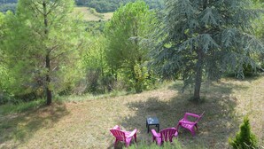 A grassy outdoor area with three pink Adirondack chairs and a small table, surrounded by trees and hills in the background. - Vacation rental for 3 people, 1 bedroom, pool, nature and peace and quiet guaranteed (Laurac)