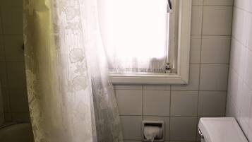 Een kleine badkamer met een toilet, een raam met gordijn en een betegelde muur.