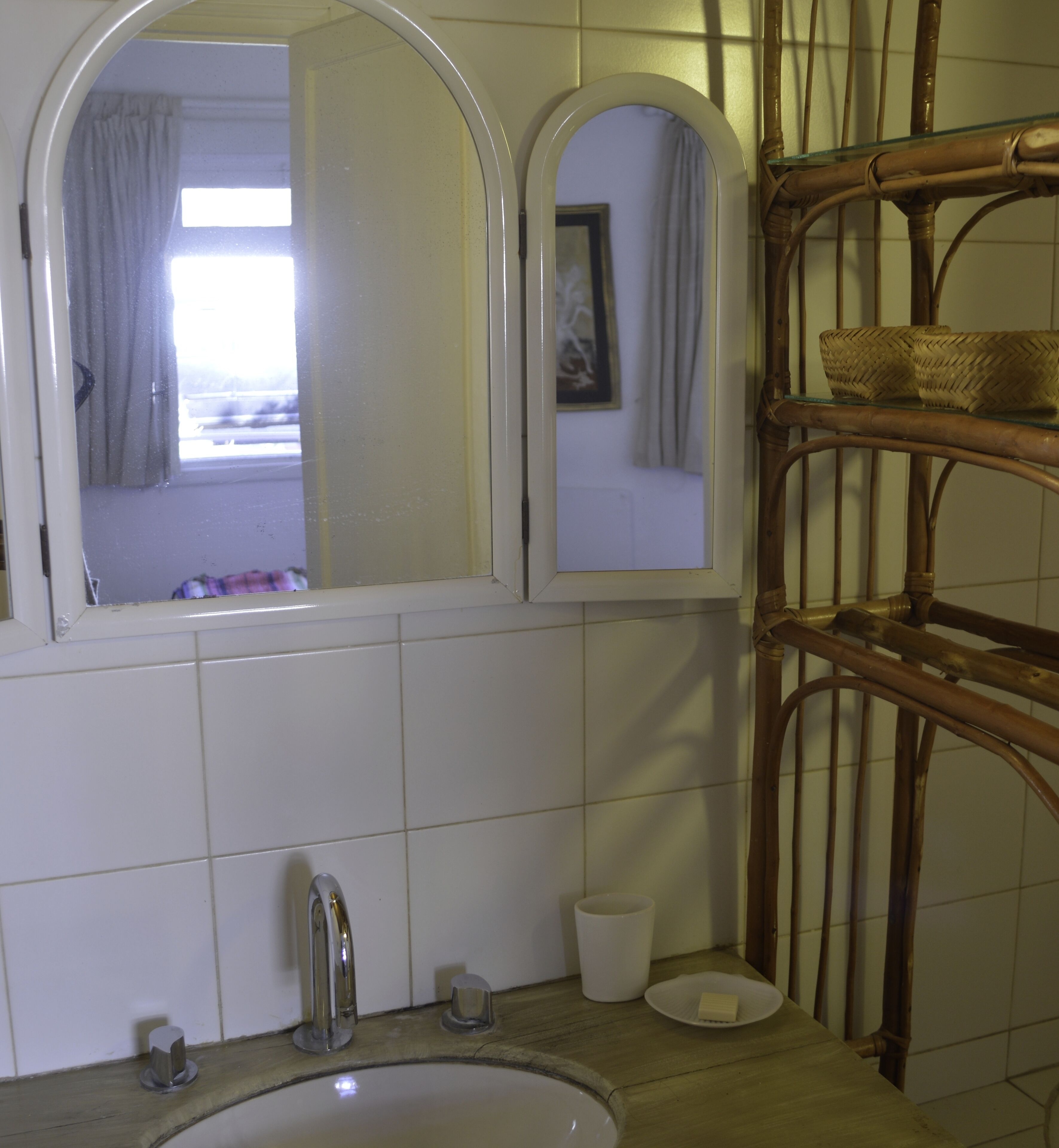 A bathroom with a white sink, a mirror, and a wicker shelf.