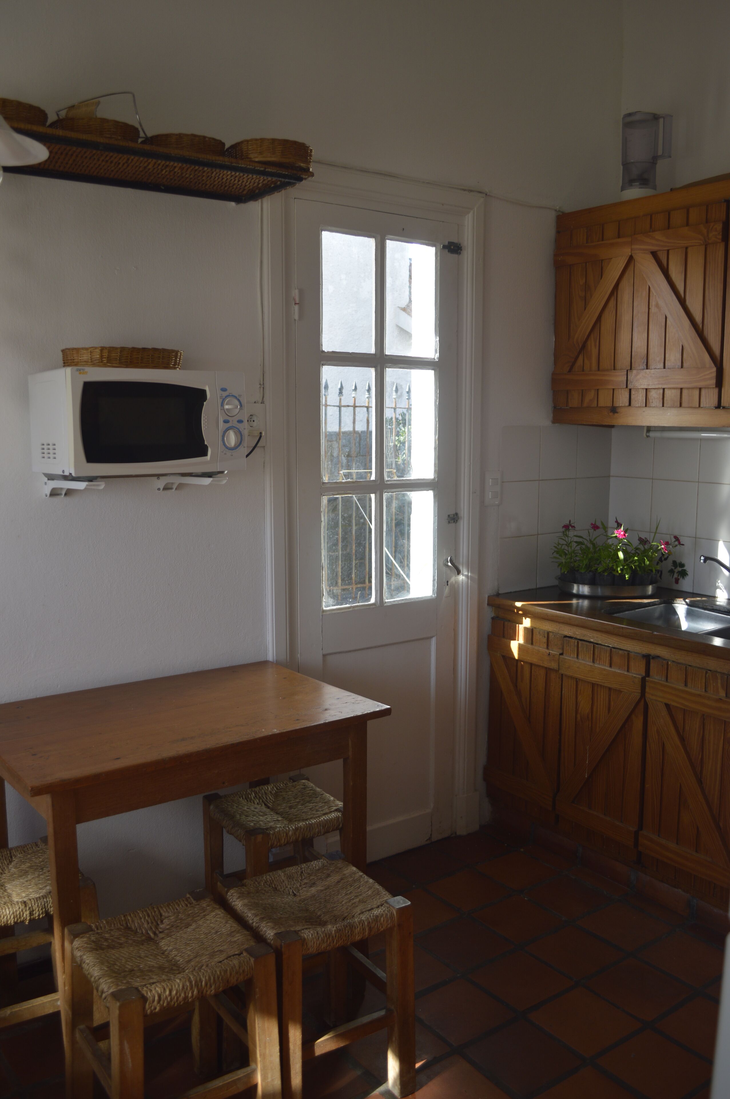 Cozinha compacta com porta branca, micro-ondas, mesa de madeira e cadeiras de vime.