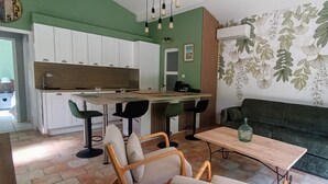 A compact living space with a kitchenette, a dining area with bar stools, a sofa, and a decorative wall with a leaf pattern. - Air-conditioned gîte in Provence near Avignon, Arles, Saint Rémy de Provence, Nîmes  (Boulbon)