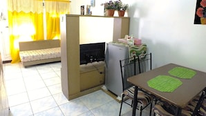 A compact living space with a sofa, a dining table with chairs, a refrigerator, and a small kitchen area.
