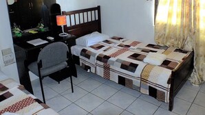 A small, tidy room with a single bed, a desk with a chair, a mirror, and a window with curtains.