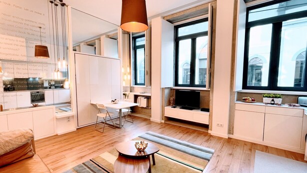 Una sala moderna con sofá, una mesa de comedor y una zona de cocina con televisor.