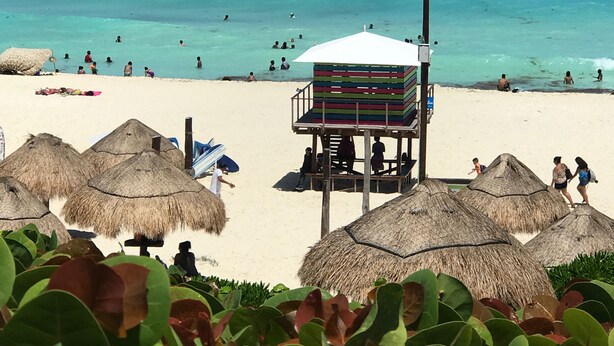 A beach with thatched umbrellas, a lifeguard tower, and clear turquoise water. - Playa del Carmen in the Riviera Maya Exclusive Condo w/ golf course & beach club (Playa del Carmen)
