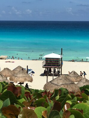 Uma praia com guarda-sóis de palha, uma torre de salva-vidas e águas turquesa cristalinas.
