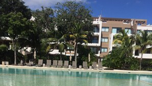 A clear pool with a large rock in the foreground, surrounded by lounge chairs and umbrellas, with a modern building in the background. - Playa del Carmen in the Riviera Maya Exclusive Condo w/ golf course & beach club (Playa del Carmen)