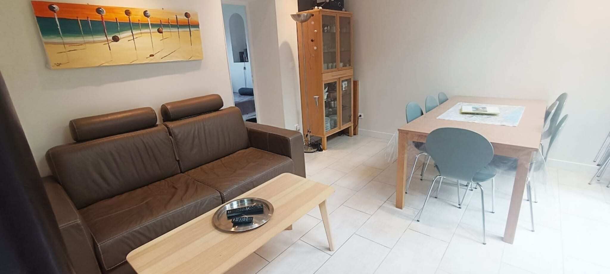 A living room with a brown sofa, a wooden coffee table, and a dining area with a wooden table and chairs.