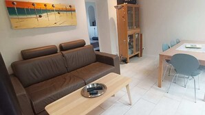 A living room with a brown sofa, a wooden coffee table, and a dining area with a wooden table and chairs. - Les Muguets Residence - Ground-Floor Apartment (Villers-sur-Mer)