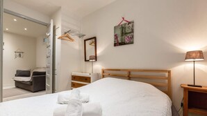 A neatly made bed with a white duvet and rolled towels, a wooden headboard, a bedside table with a lamp, a small bedside drawer, a mirror, and a wall-mounted picture. - Les Muguets Residence - Ground-Floor Apartment (Villers-sur-Mer)