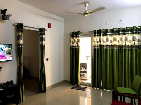 Una sala de estar con televisor, ventilador de techo y cortinas.