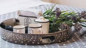 A tray with mugs and a plant on a bed with a polka dot bedspread.