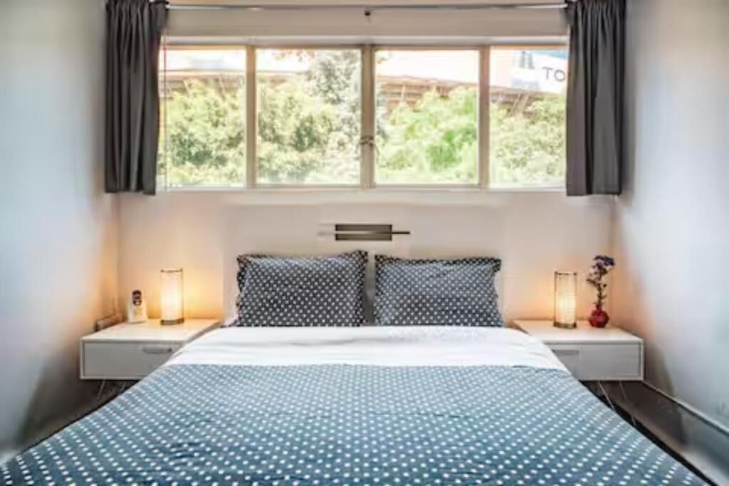 A bedroom with a bed, two bedside tables, a window with curtains, and a view of greenery outside.