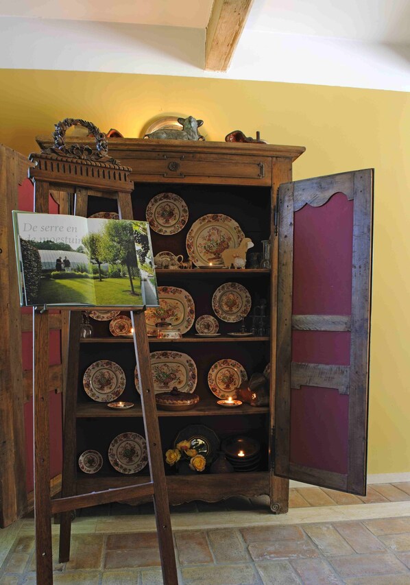 A rustic wooden cabinet with shelves holding decorative plates and a candle, next to an open book on an easel. - Beautiful countryhouse in rural surroundings with pool and pool house. (Grignan (Drome Provencale))