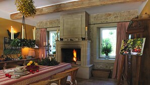 A cozy room with a fireplace, dining table, wicker chairs, and a painting on the wall. - Beautiful  countryhouse in rural surroundings with pool and pool house.   (Grignan (Drome Provencale))