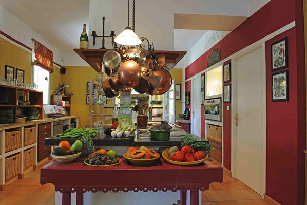 A kitchen with a central island, various fruits and vegetables, and hanging copper pots.