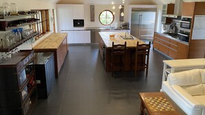 Cozinha moderna com ilha central, armários de madeira e área de jantar com sofá branco e mesa de xadrez.