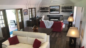 Uma sala de estar moderna com um sofá branco, almofadas vermelhas, uma mesa de centro e uma lareira. Há prateleiras com copos e um quadro na parede.