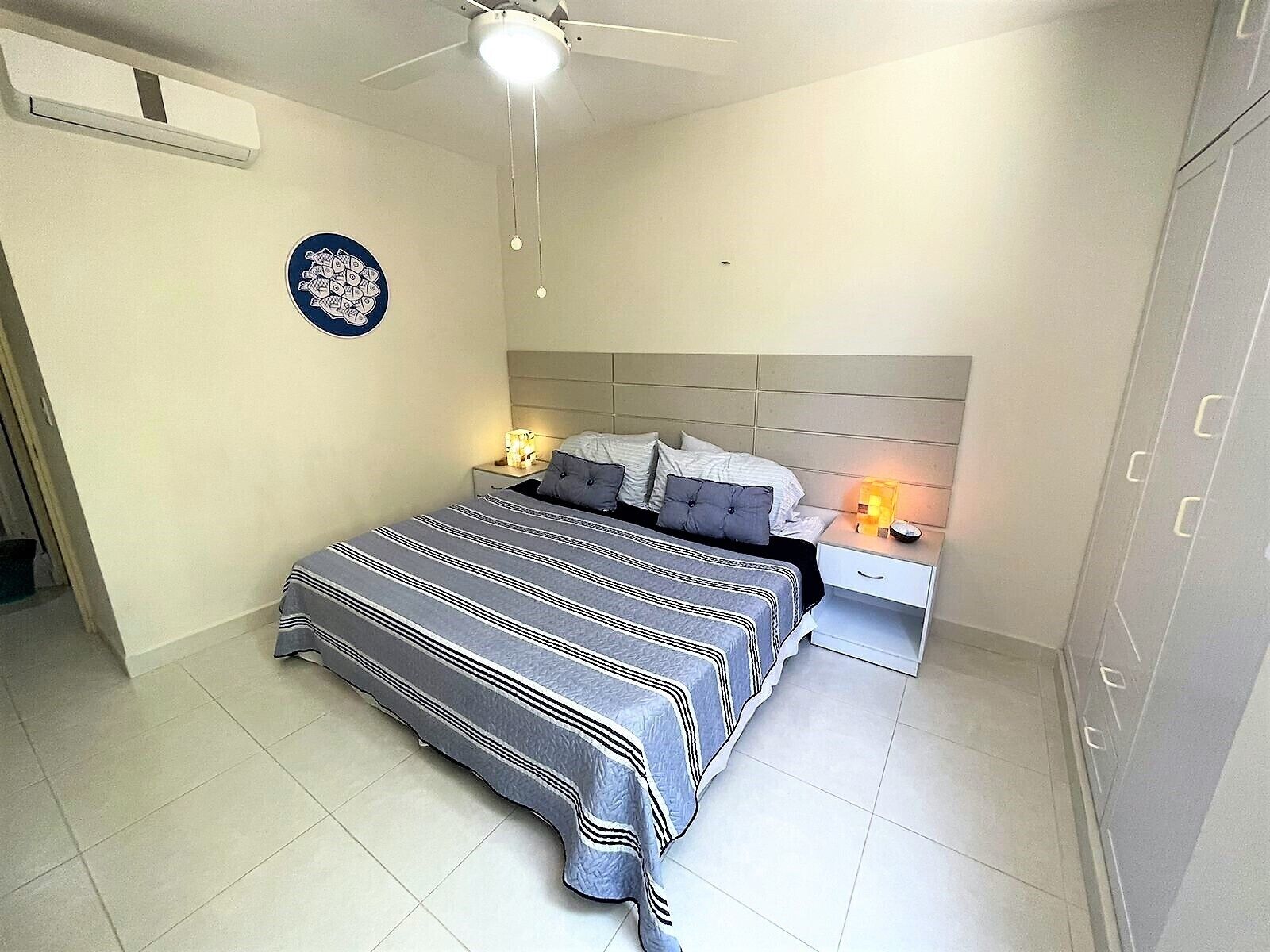 A bedroom with a bed, nightstands, a ceiling fan, and a wall-mounted air conditioning unit.