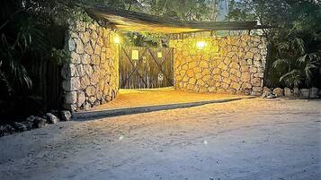 A stone-walled entrance with a covered pathway leading to a building, surrounded by greenery.