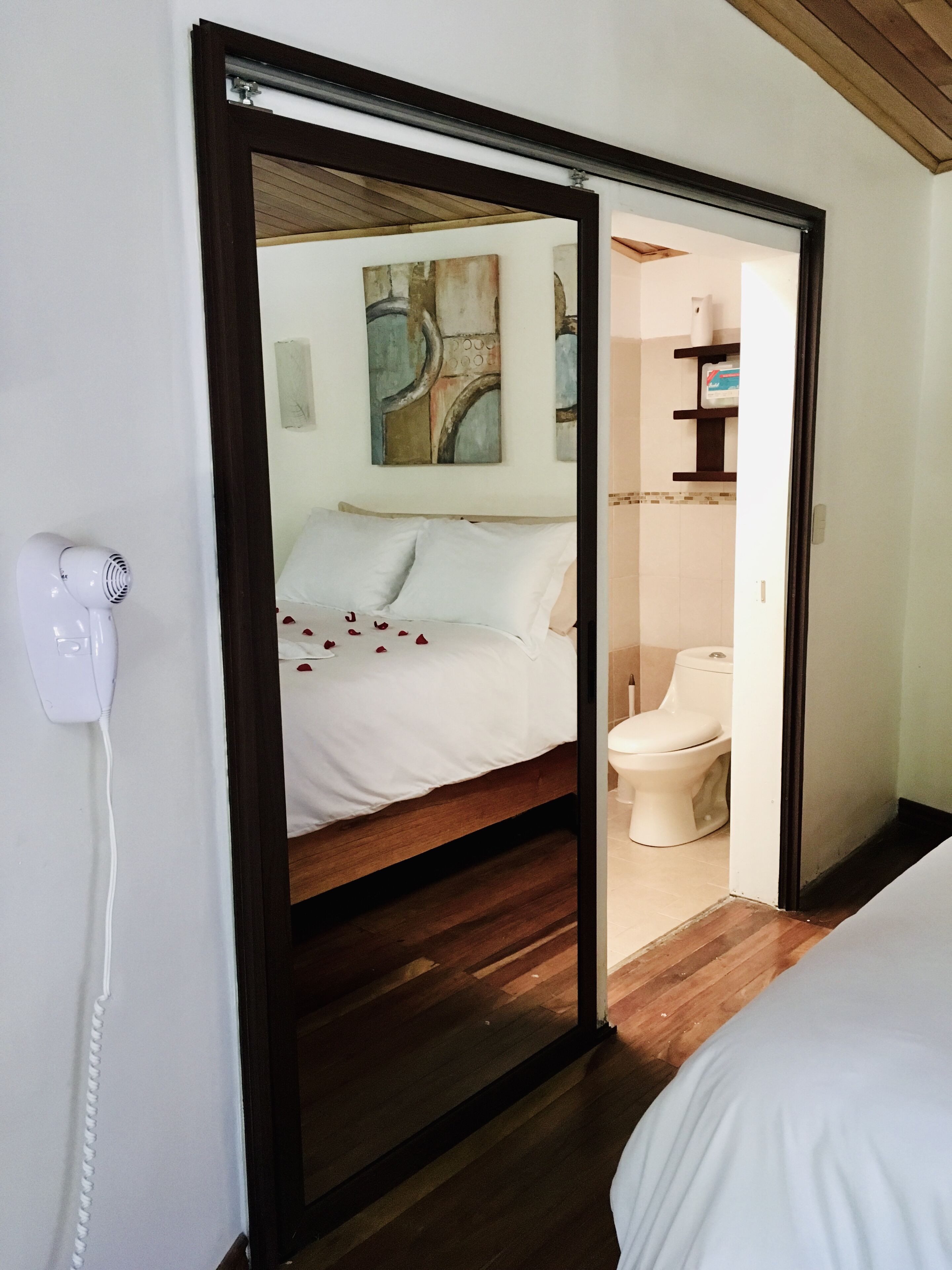 Un dormitorio con cama, teléfono en la mesita de noche y baño visible a través de una puerta abierta.