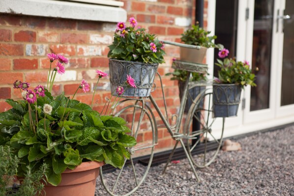 Potted plants on a metal bicycle wheel planter against a brick wall.