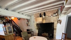 Een gezellige woonkamer met een open haard, een bank, een ronde tafel en een trap naar een hoger gelegen verdieping.